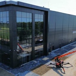 Eskaro - Nowoczesny budynek biurowy z szklaną fasadą i spider liftem, zaparkowane pojazdy, widok z góry na plac budowy z elementami rusztowania.