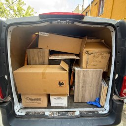 Expressfix - Wnętrze busa wypełnione kartonami i elementami drewnianymi, prawdopodobnie podczas przeprowadzki lub transportu mebli. Widoczne różne marki na opakowaniach.