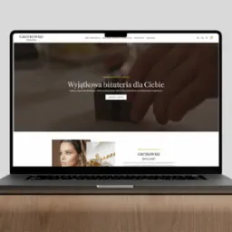 Laptop wyświetla stronę internetową Grotkowski Jewellery z ofertą biżuterii: złoto, srebro, perły i kamienie szlachetne. Minimalistyczny design strony z elegancką typografią.