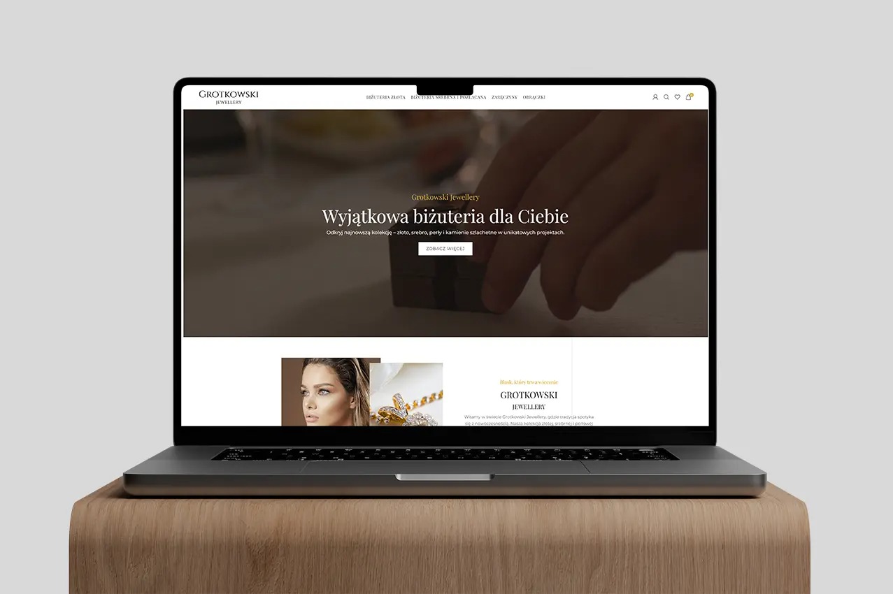 Laptop wyświetla stronę internetową Grotkowski Jewellery z ofertą biżuterii: złoto, srebro, perły i kamienie szlachetne. Minimalistyczny design strony z elegancką typografią.