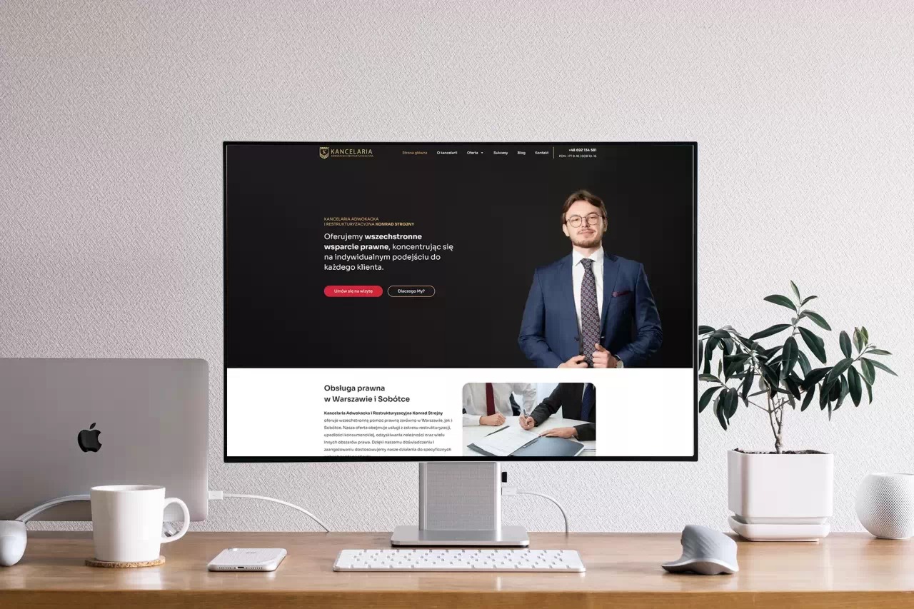 Ekran monitora wyświetla stronę internetową kancelarii adwokackiej. Minimalistyczne biurko z rośliną i akcesoriami Apple tworzy profesjonalne tło.