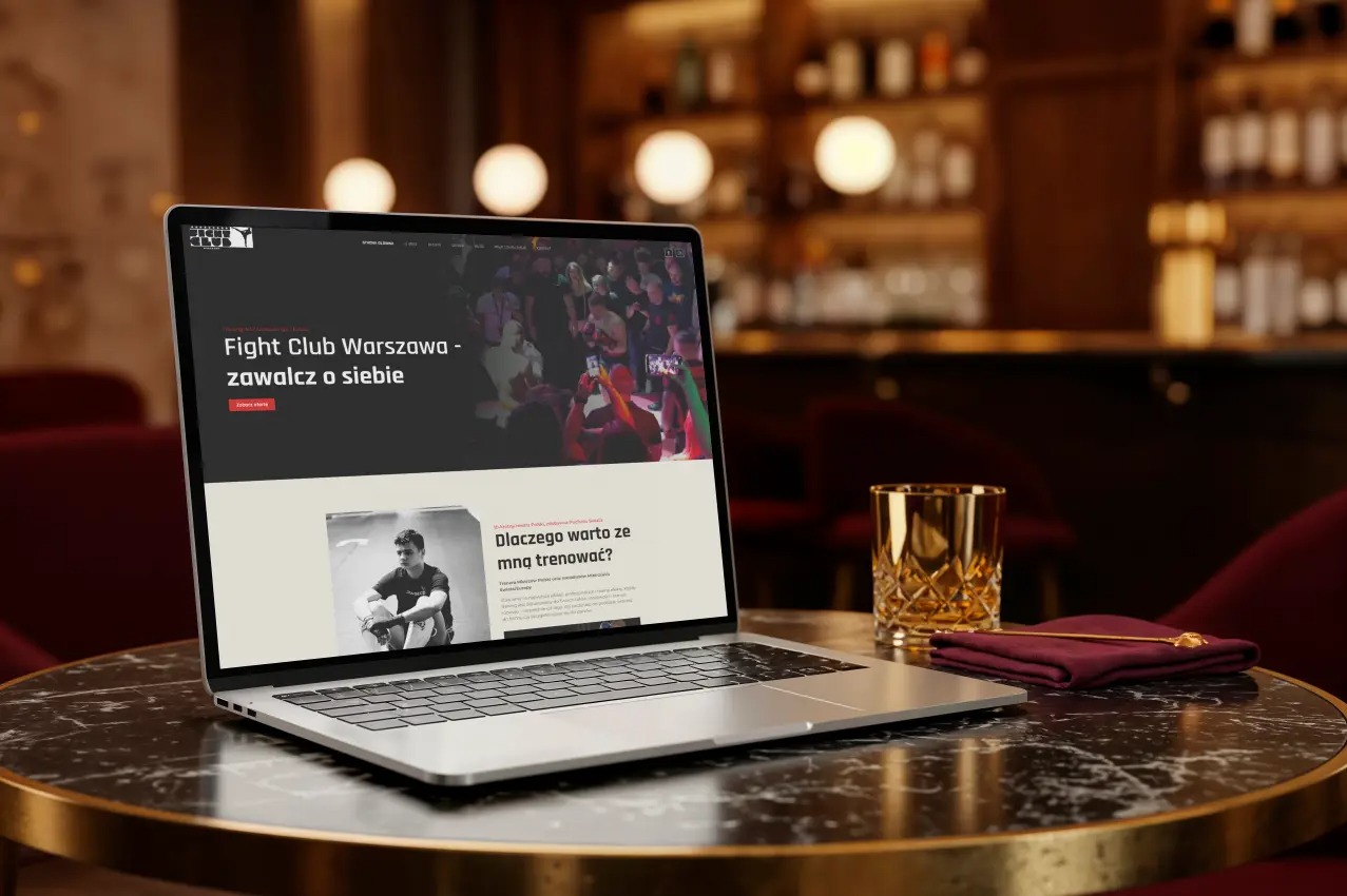 Laptop prezentuje stronę 'Fight Club Warszawa' na marmurowym stoliku w barze, z kieliszkiem i serwetką obok.