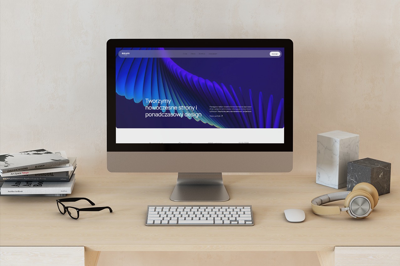 Monitor iMac prezentuje nowoczesną stronę internetową z fioletowo-niebieską grafiką. Na biurku książki, okulary, klawiatura, mysz i słuchawki.