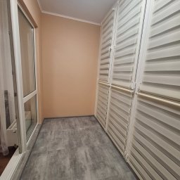 BOT - Wykończony balkon z szarymi płytkami podłogowymi, białymi oknami i roletami w kolorze ecru, tworzącymi nowoczesny i minimalistyczny wygląd.