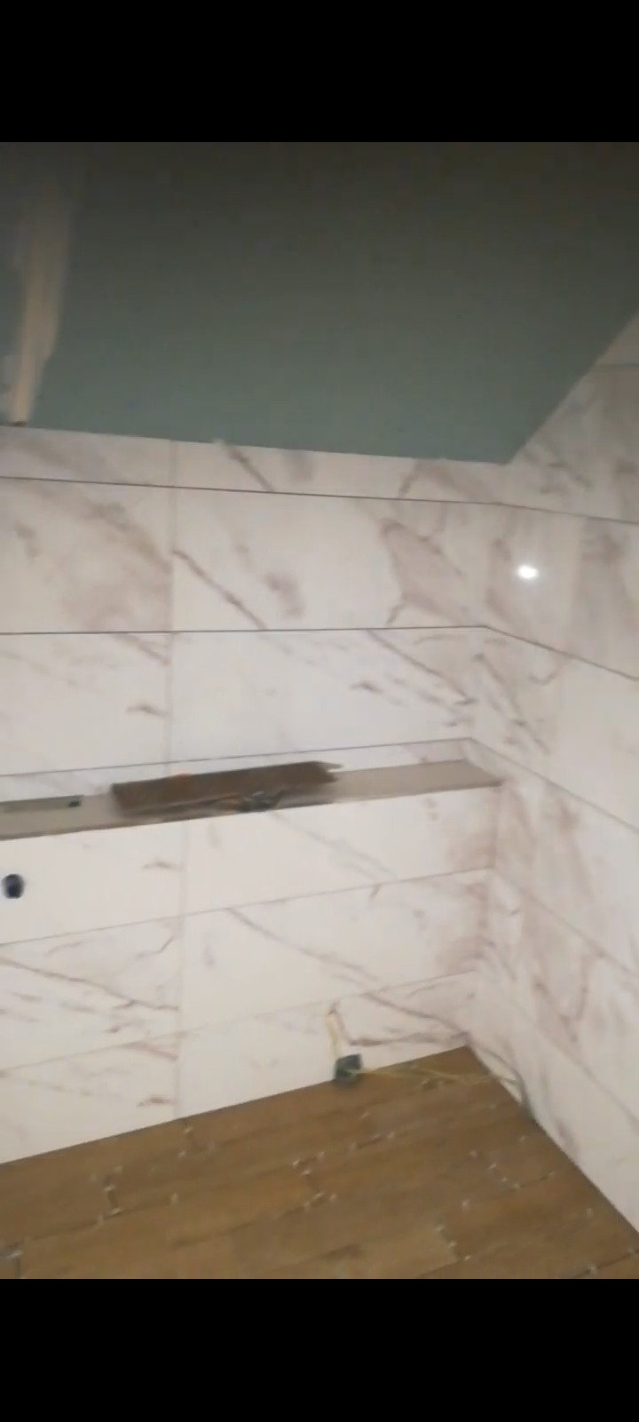 Łazienka w trakcie wykończenia: marmurowe płytki na ścianach, drewnopodobne na podłodze, sufit z płyty KG. Widoczne niedokończone prace.