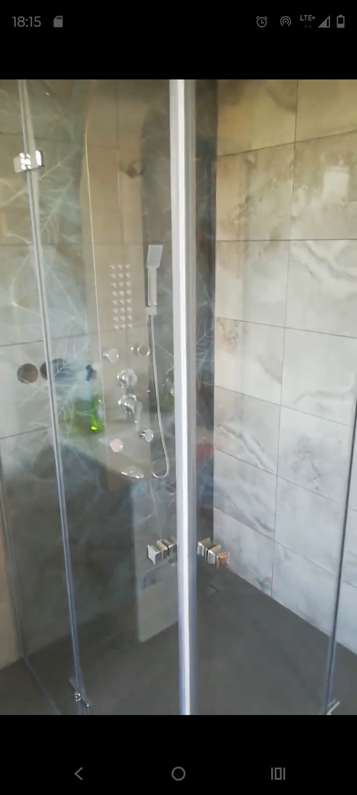 Nowoczesna kabina prysznicowa z panelem hydromasażu, wykończona płytkami imitującymi marmur. Chromowane detale i szklane drzwi.