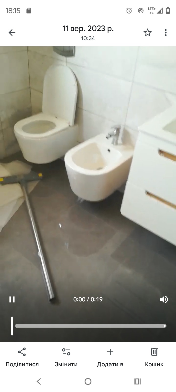 Nowoczesna łazienka po remoncie: biała toaleta, bidet i szafka, szara podłoga z połyskiem. Widoczny fragment mopa. Świeżo po pracach wykończeniowych.