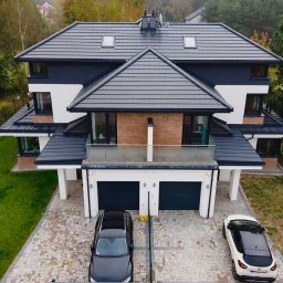 RAVEN S.C. KRZYSZTOF BOŚKA, SŁAWOMIR BŁASZCZAK - Nowoczesny dom dwupiętrowy z ciemną dachówką i oknami, balkon z przeszkloną balustradą, dwa samochody na brukowanym podjeździe, widok z góry.