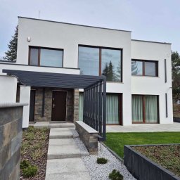 RAVEN S.C. KRZYSZTOF BOŚKA, SŁAWOMIR BŁASZCZAK - Nowoczesny dom z dużymi oknami, drewnianymi ramami i minimalistycznym designem. Wejście zdobi pergola i kamienne wykończenie.