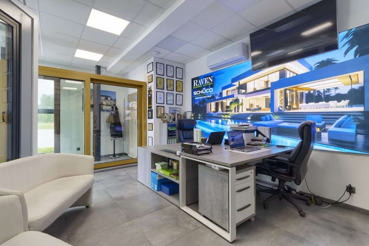 Biuro z ekspozycją drzwi przesuwnych i okien. Na ścianie grafika z nowoczesnym domem z basenem. W tle rama z certyfikatami.