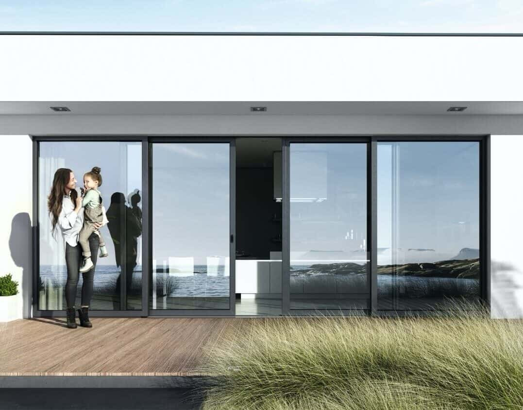 Eleganckie, szklane drzwi przesuwne z widokiem na morze. Kobieta z dzieckiem na tarasie z drewnianą podłogą. Minimalistyczny design i naturalne światło.