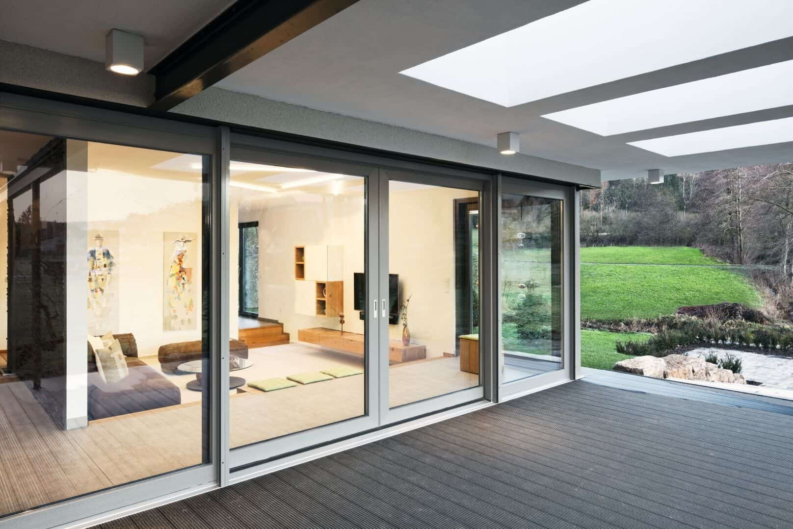 Nowoczesne drzwi przesuwne tarasowe, szare ramy, widok na salon i ogród. Minimalistyczny design, drewniany taras.