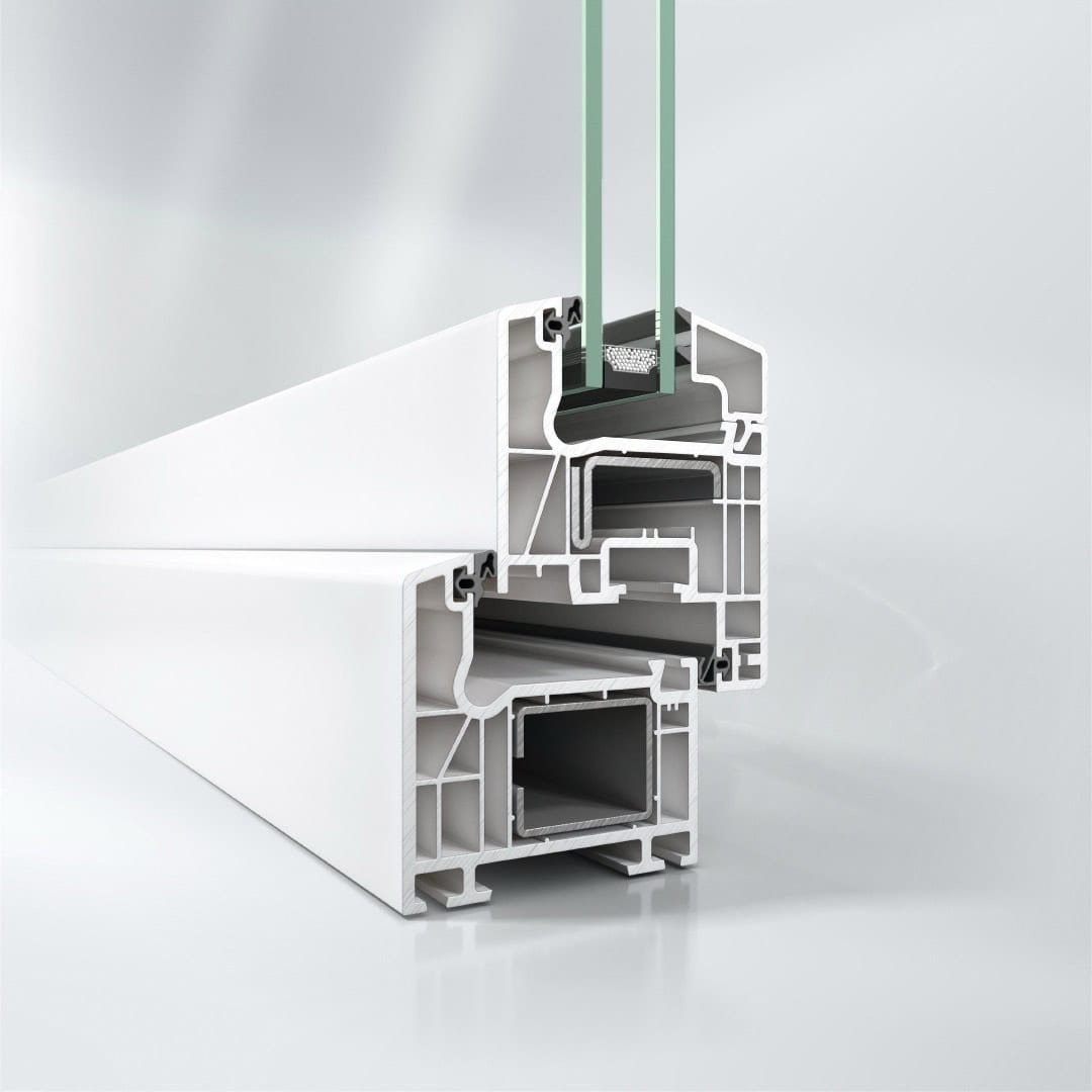 Przekrój profilu okiennego PCV z szybą zespoloną, ukazujący wewnętrzną strukturę i komory izolacyjne. Białe tworzywo sztuczne, szare uszczelki, szkło w neutralnym odcieniu.