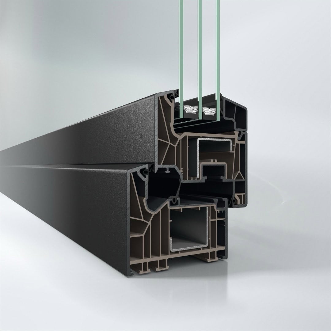 Przekrój ramy okiennej z trzema szybami, ukazujący wielokomorową konstrukcję profili i uszczelnień w odcieniach brązu i czerni na jasnym tle.