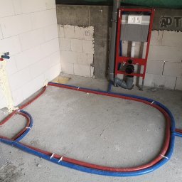 AD Tech Andrzej Drzazga - Instalacja ogrzewania podłogowego w łazience, rury czerwone i niebieskie ułożone na surowym betonie, widoczne elementy montażowe we Wrocławiu.