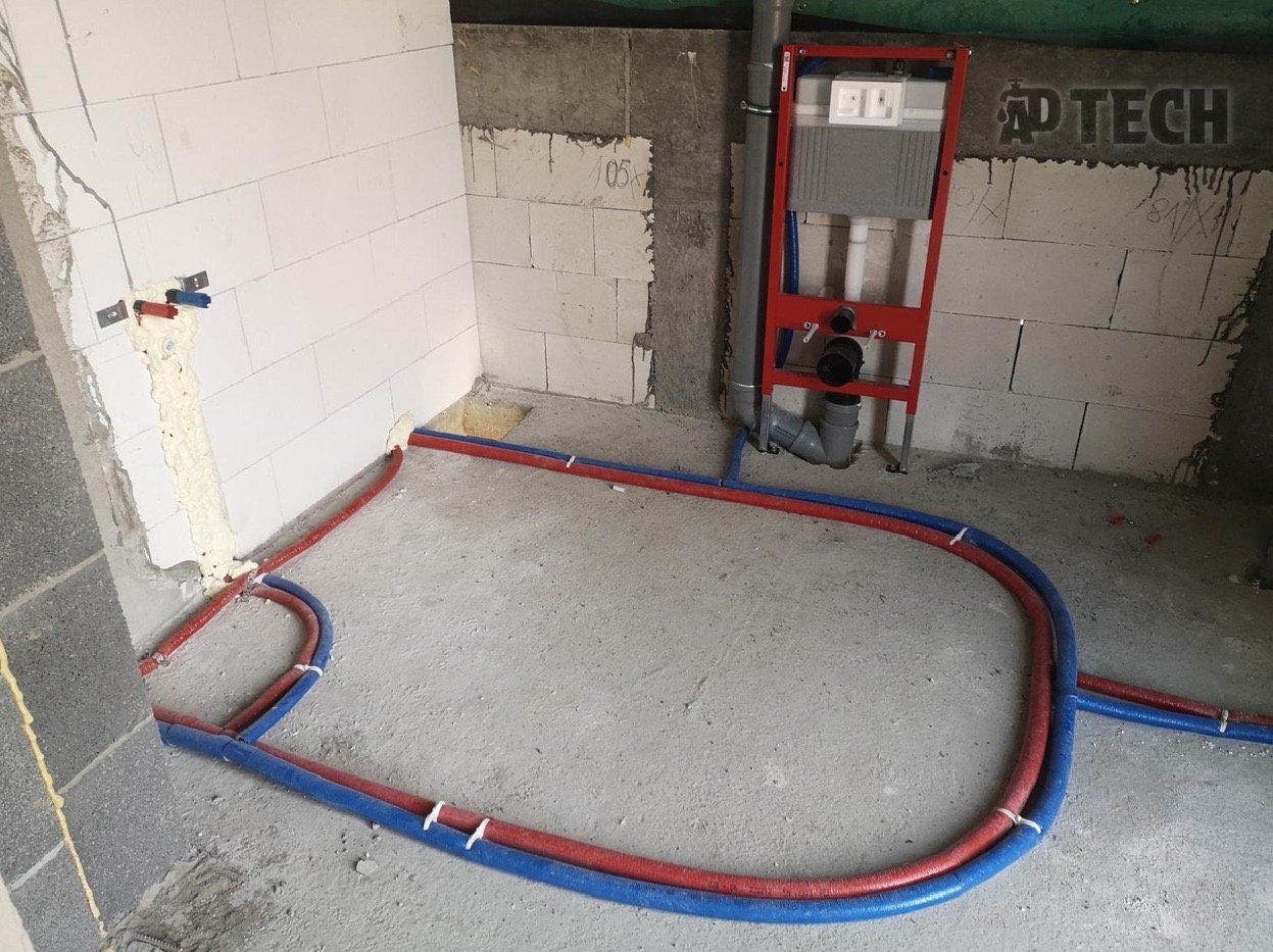 Instalacja ogrzewania podłogowego w łazience, rury czerwone i niebieskie ułożone na surowym betonie, widoczne elementy montażowe we Wrocławiu.