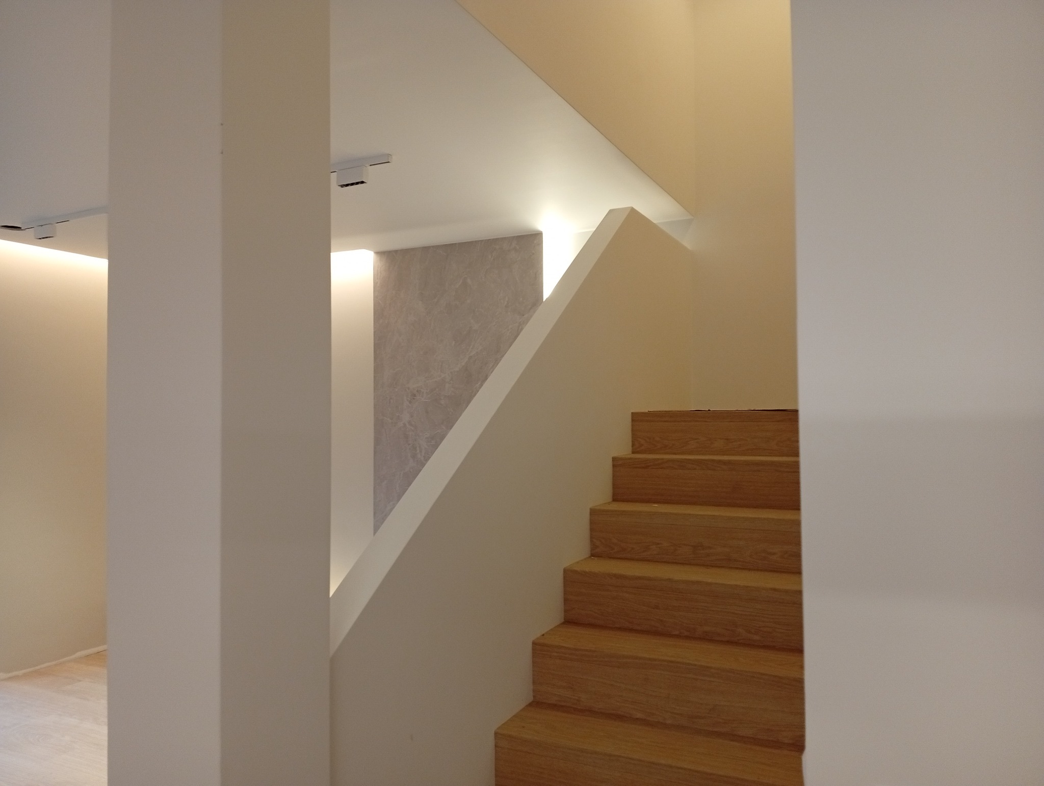 Nowoczesne schody drewniane z białymi ścianami i subtelnym oświetleniem LED. Minimalistyczny design, gładkie powierzchnie, ciepłe odcienie drewna i bieli. Wykończenie wnętrz.