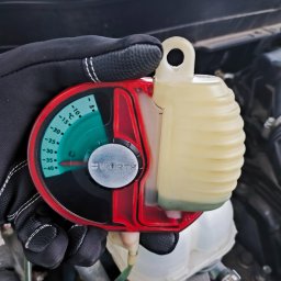 MICHAŁ KOWALÓWKA M&M BROKERS - Pomiar temperatury płynu chłodniczego w samochodzie za pomocą refraktometru marki Wurth, trzymanego w rękawicy ochronnej na tle silnika.