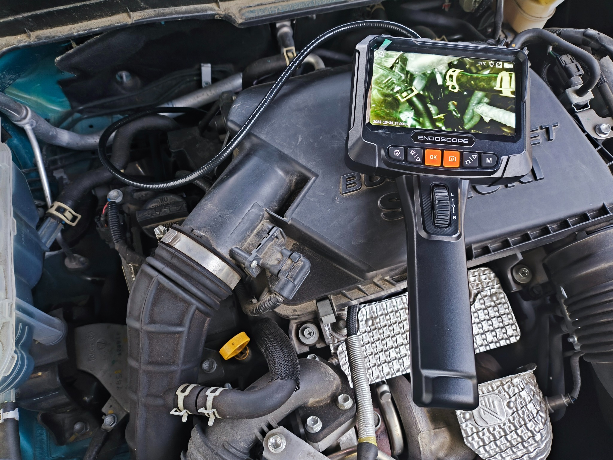 Silnik samochodu sprawdzany endoskopem. Na ekranie urządzenia widoczne wnętrze silnika. Diagnostyka pojazdu, kontrola stanu technicznego. Czarny wąż endoskopu.