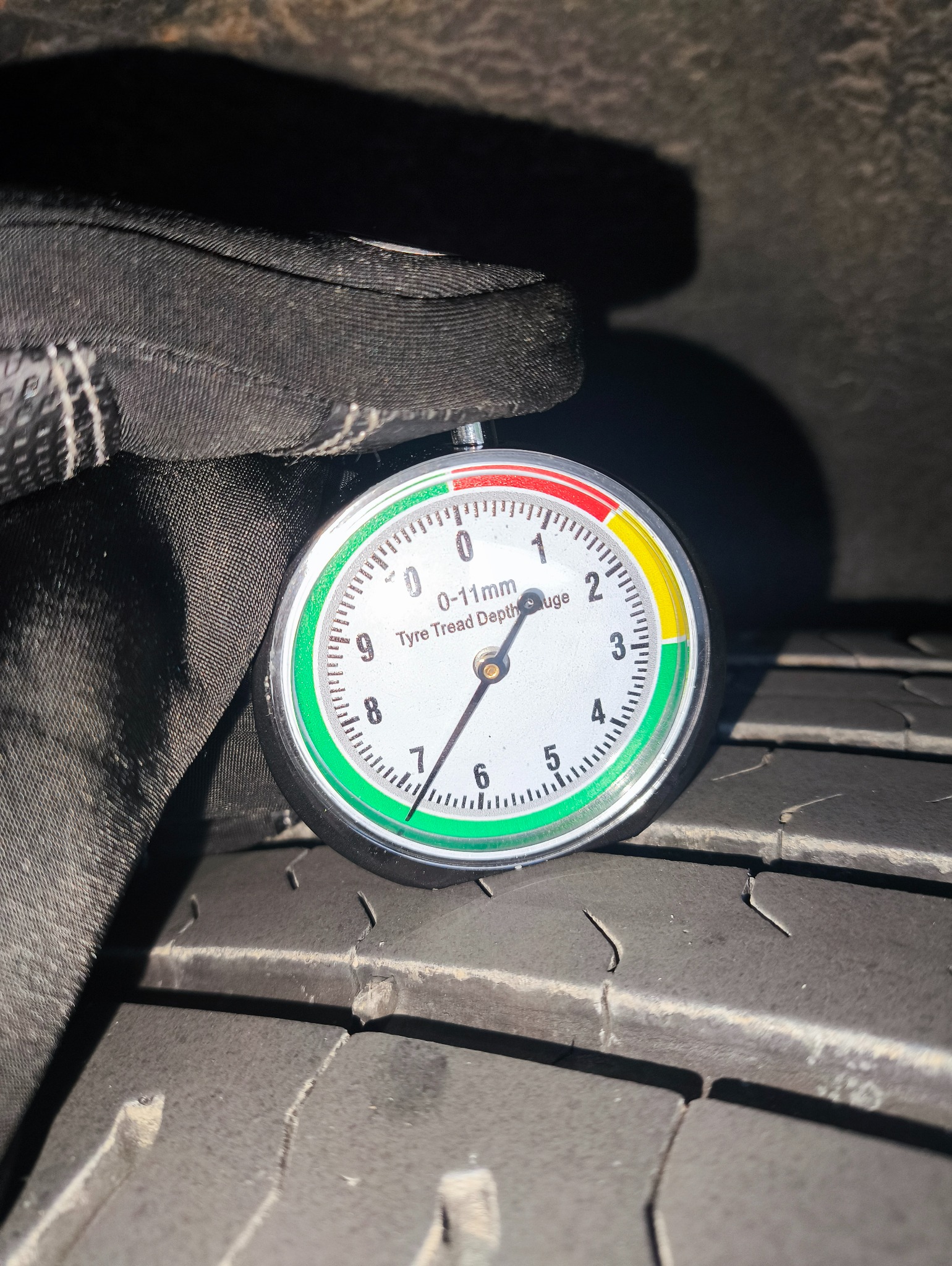 Pomiar głębokości bieżnika opony samochodowej za pomocą specjalistycznego miernika. Wskazanie na granicy strefy żółtej, opona w trakcie użytkowania.