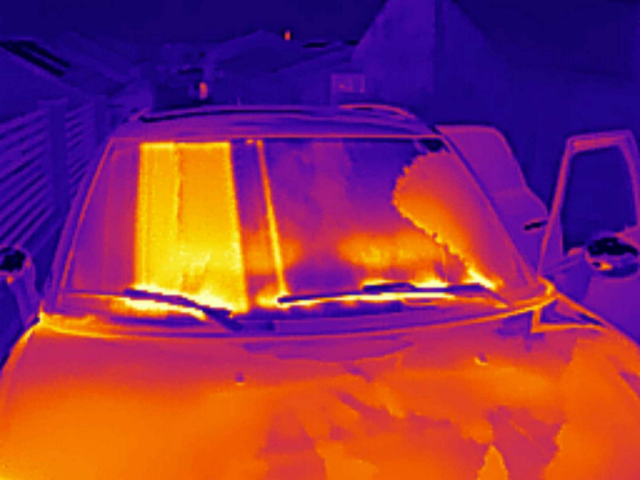 Termowizyjne zdjęcie samochodu z otwartymi drzwiami, ukazujące rozkład temperatury na szybie przedniej i karoserii, wykonane w odcieniach pomarańczy i fioletu.
