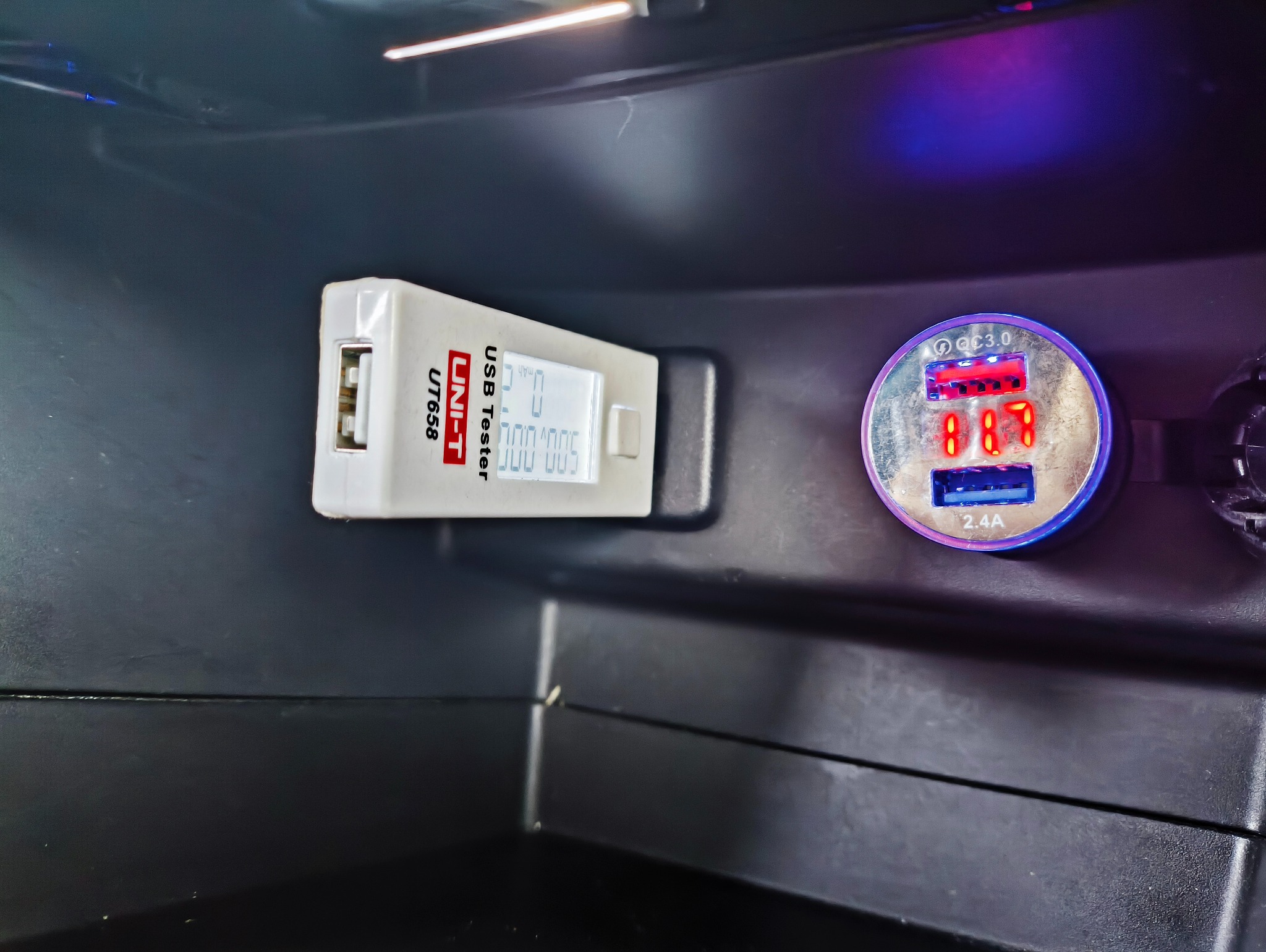 Tester USB UNIT-T UT658 podłączony do ładowarki samochodowej, wyświetlający parametry ładowania w ciemnym wnętrzu pojazdu.