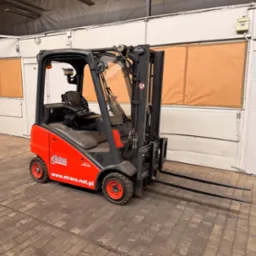 Czerwono-szary wózek widłowy Linde z otwartą kabiną na tle magazynu z oknami zabezpieczonymi brązowym papierem. Na wózku widoczne logo firmy etrans.net.pl.