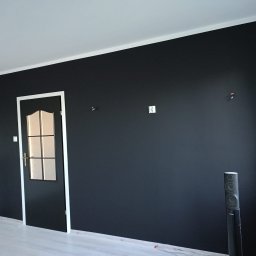 Angelika Krause - Ściana pomalowana na czarno z białą stolarką drzwiową i przypodłogową. Widoczne głośniki pod ścianą. Minimalistyczny design wnętrza po malowaniu.