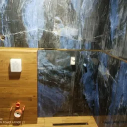 Wykończona łazienka z płytkami imitującymi marmur w odcieniach granatu i złota, zabudowa geberitu z drewnianymi panelami, widoczne przyłącza.