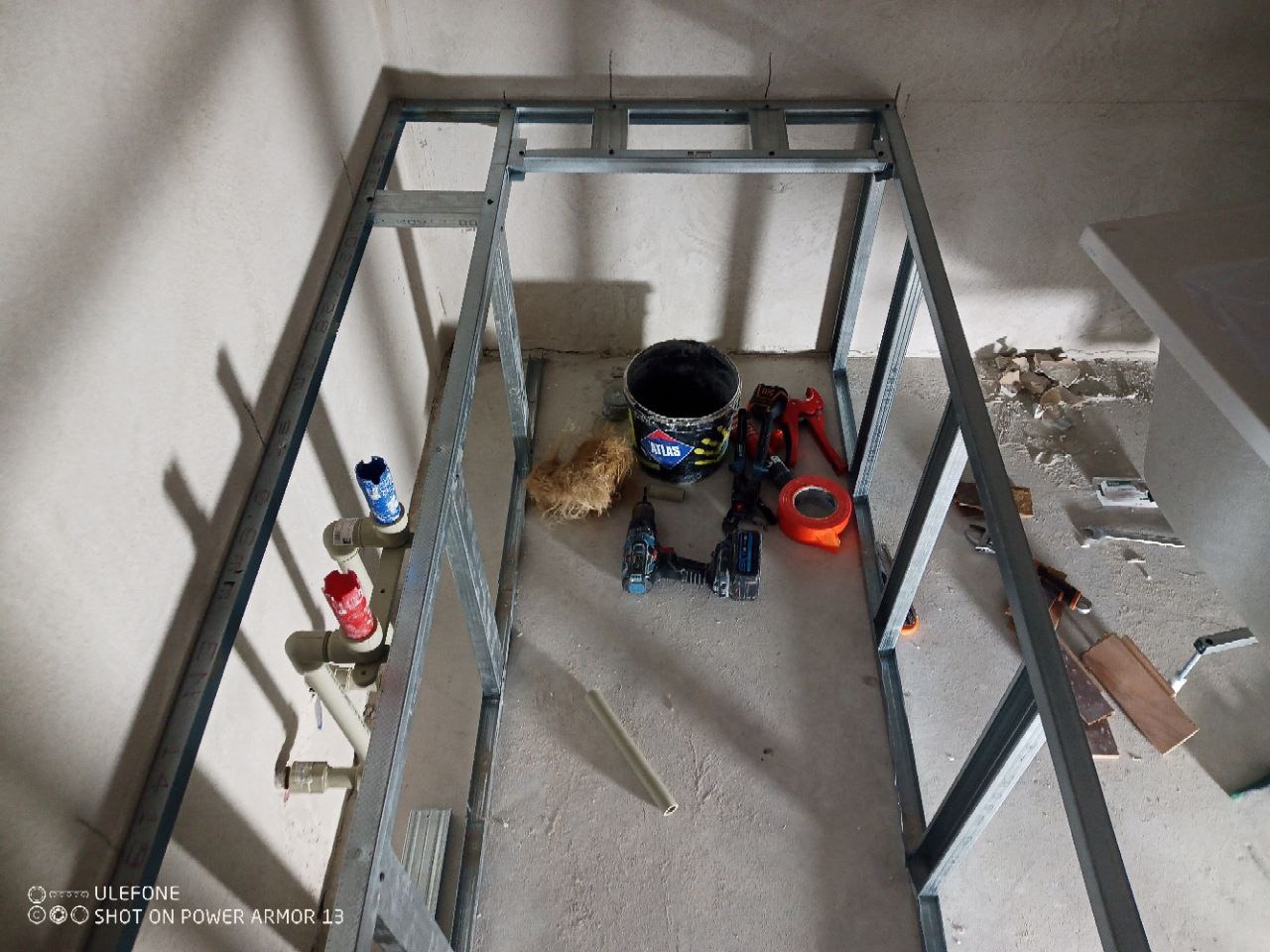 Metalowa konstrukcja pod zabudowę w łazience, widoczne narzędzia i materiały budowlane. Instalacja wodna z rurami. Etap prac wykończeniowych.