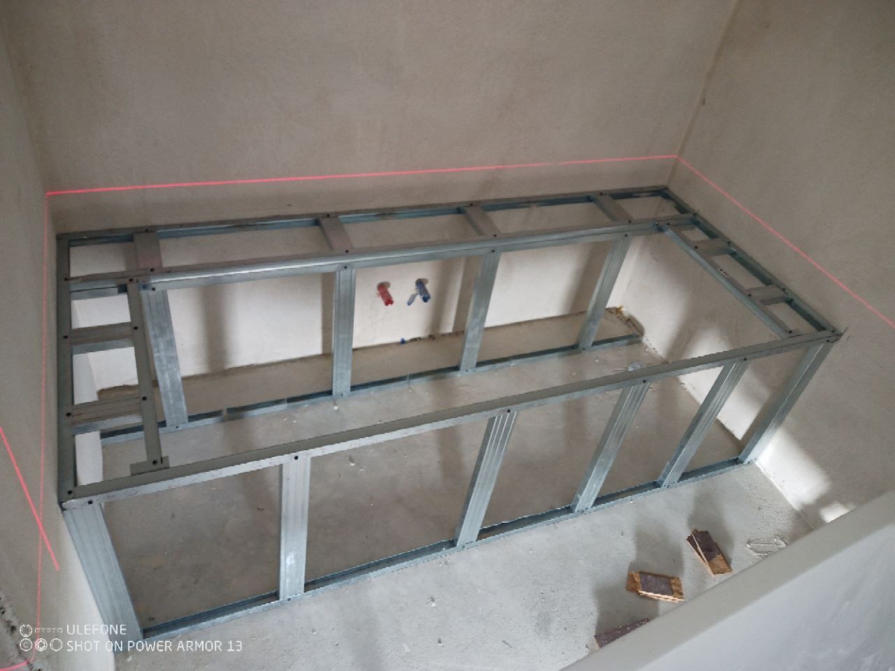Metalowy stelaż zabudowy w łazience, poziomowany laserowo, przygotowany pod płytki. Widoczne fragmenty instalacji wodnej.