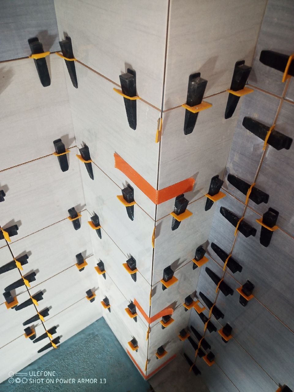 Ściana z jasnych płytek, wyrównana z użyciem klipsów i pasków dystansowych, widok z góry, ukazujący precyzję i etap prac glazurniczych.