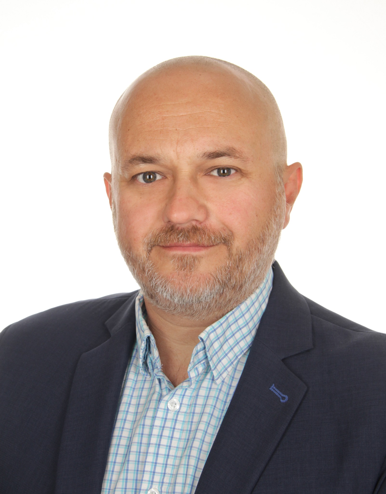Portret biznesowy: łysiejący mężczyzna z brodą, w niebieskiej marynarce i koszuli w kratę, uśmiecha się na białym tle. Widoczne detale stroju.