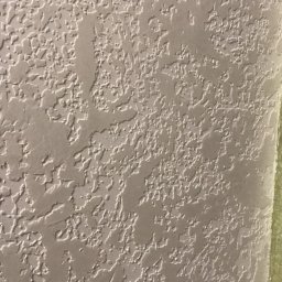 Usługi Budowlane Mykola Milientiev - Teksturowana, beżowa ściana z wyraźnym wzorem, prawdopodobnie po szpachlowaniu lub malowaniu strukturalnym. Widoczny fragment taśmy malarskiej przy krawędzi.