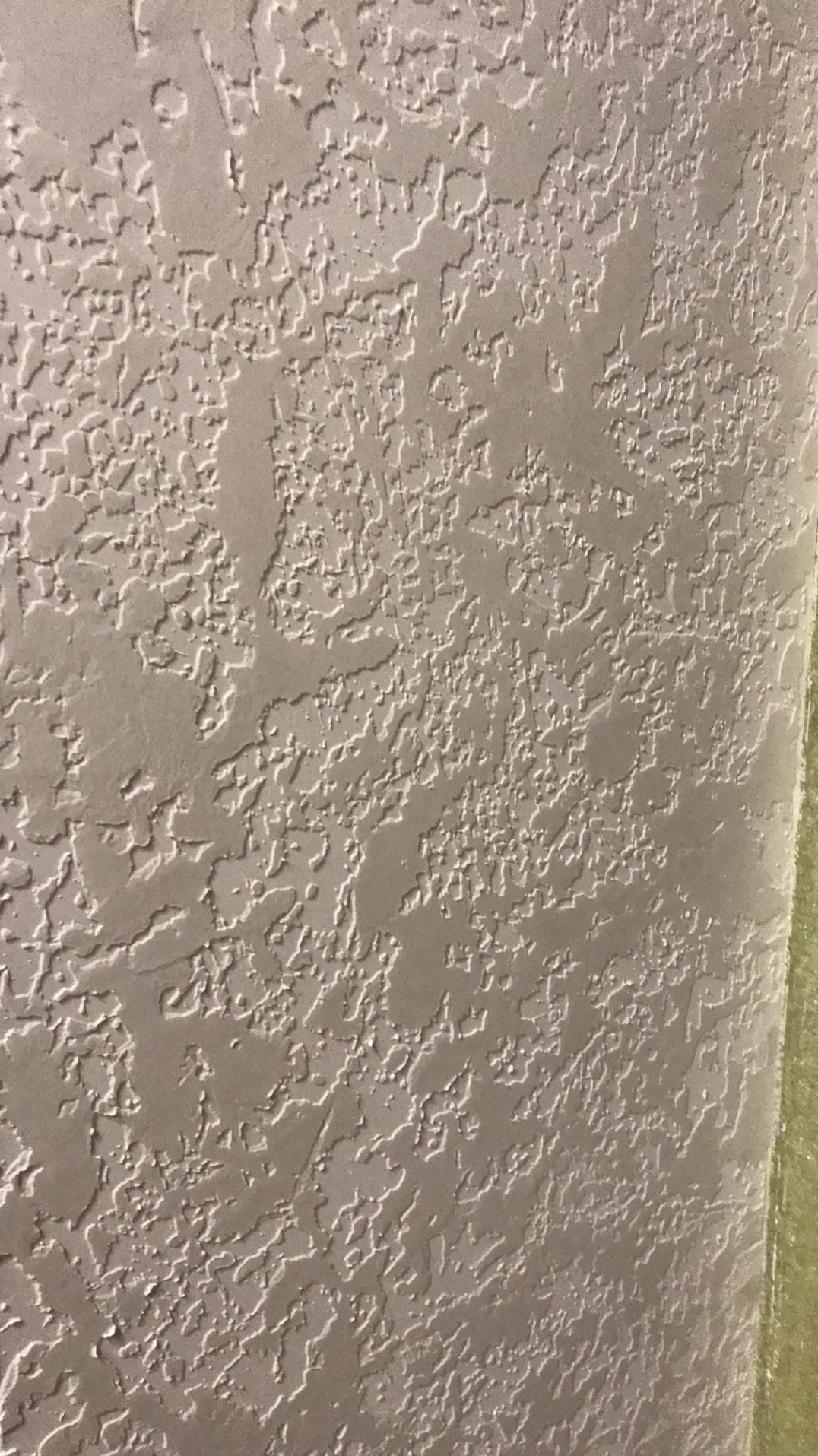 Teksturowana, beżowa ściana z wyraźnym wzorem, prawdopodobnie po szpachlowaniu lub malowaniu strukturalnym. Widoczny fragment taśmy malarskiej przy krawędzi.