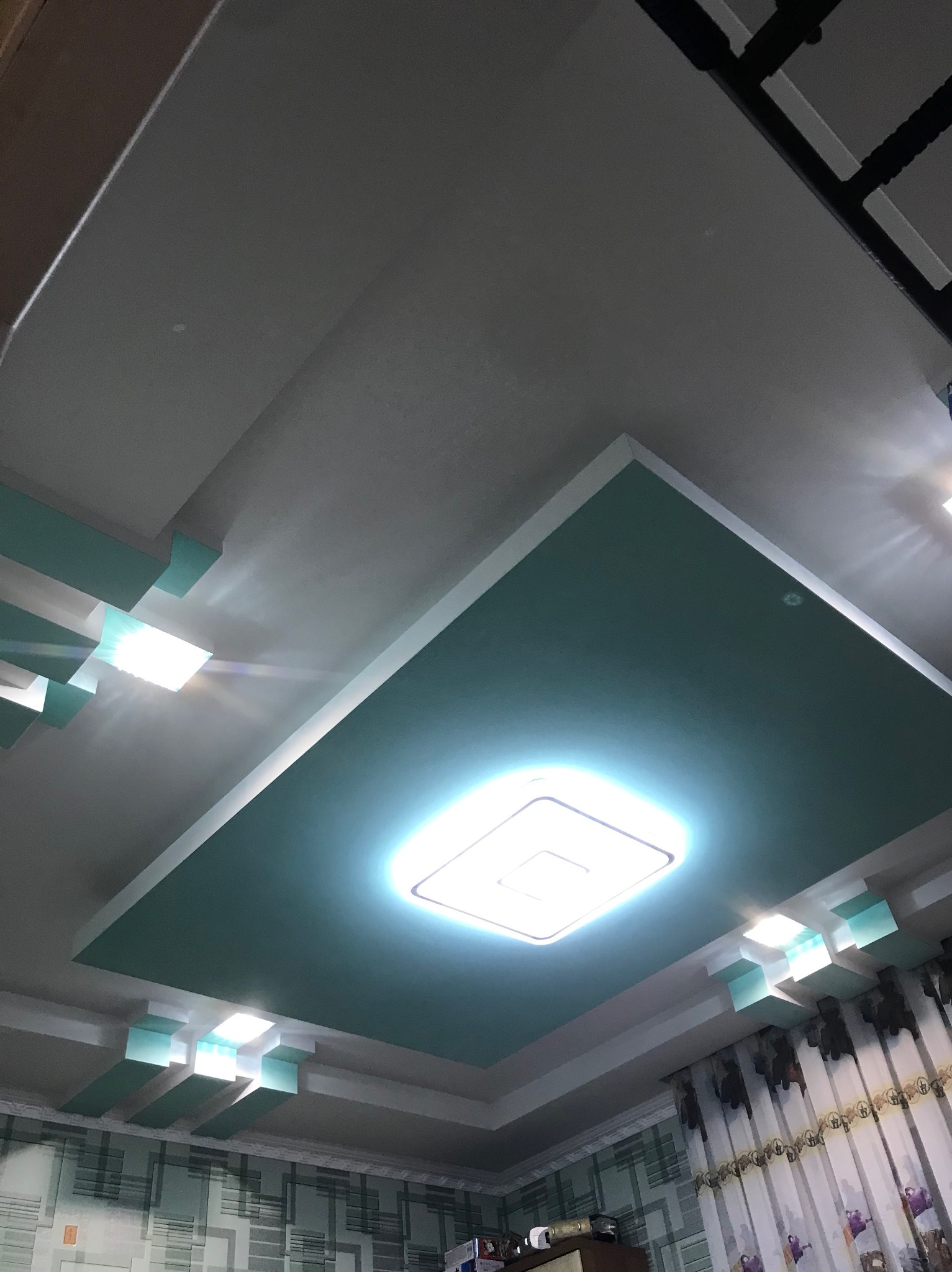 Podwieszany sufit z oświetleniem LED w kolorze turkusowym, widok z dołu, dekoracyjne wykończenie, nowoczesny design, pokój z zasłonami w tle.