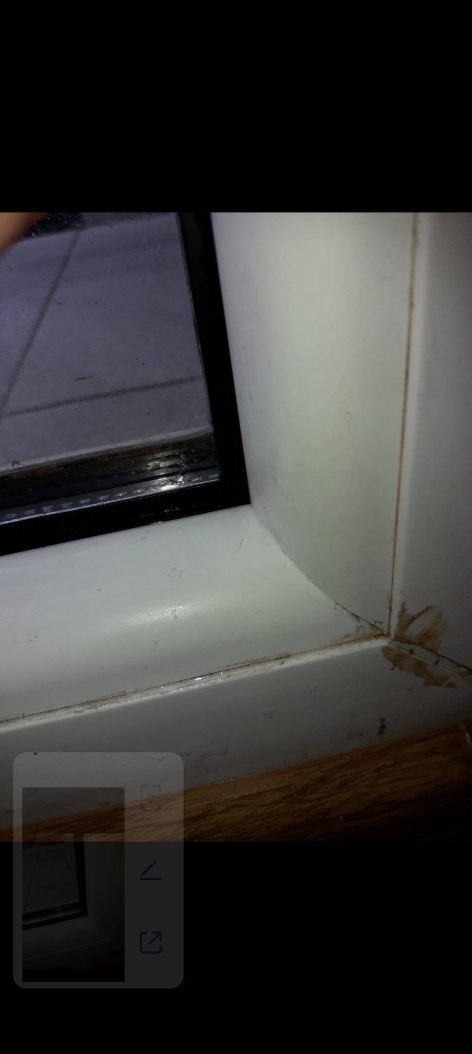 Brudne, białe ramy okienne PCV w rogu, z widocznymi zabrudzeniami i smugami. Widoczny fragment szyby i parapetu. Narożnik ramy z bliska.