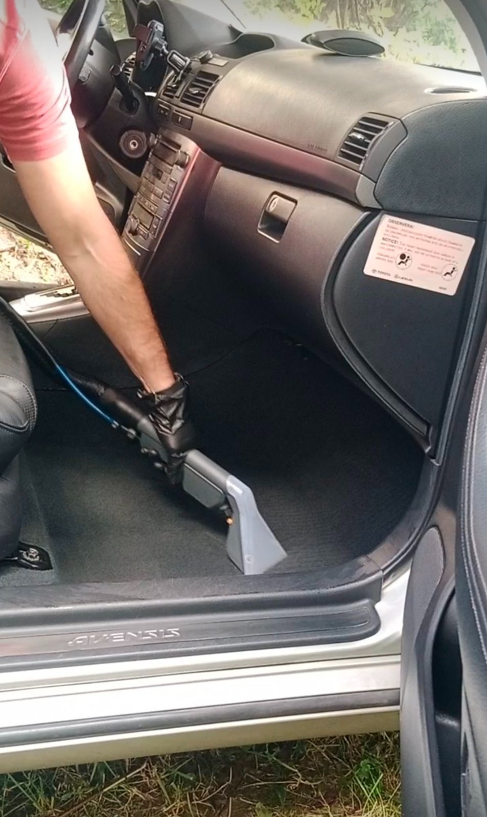 Czyszczenie podłogi samochodu odkurzaczem piorącym. Widoczny fragment wnętrza auta, wąż i ssawka odkurzacza oraz dłoń w czarnej rękawicy.