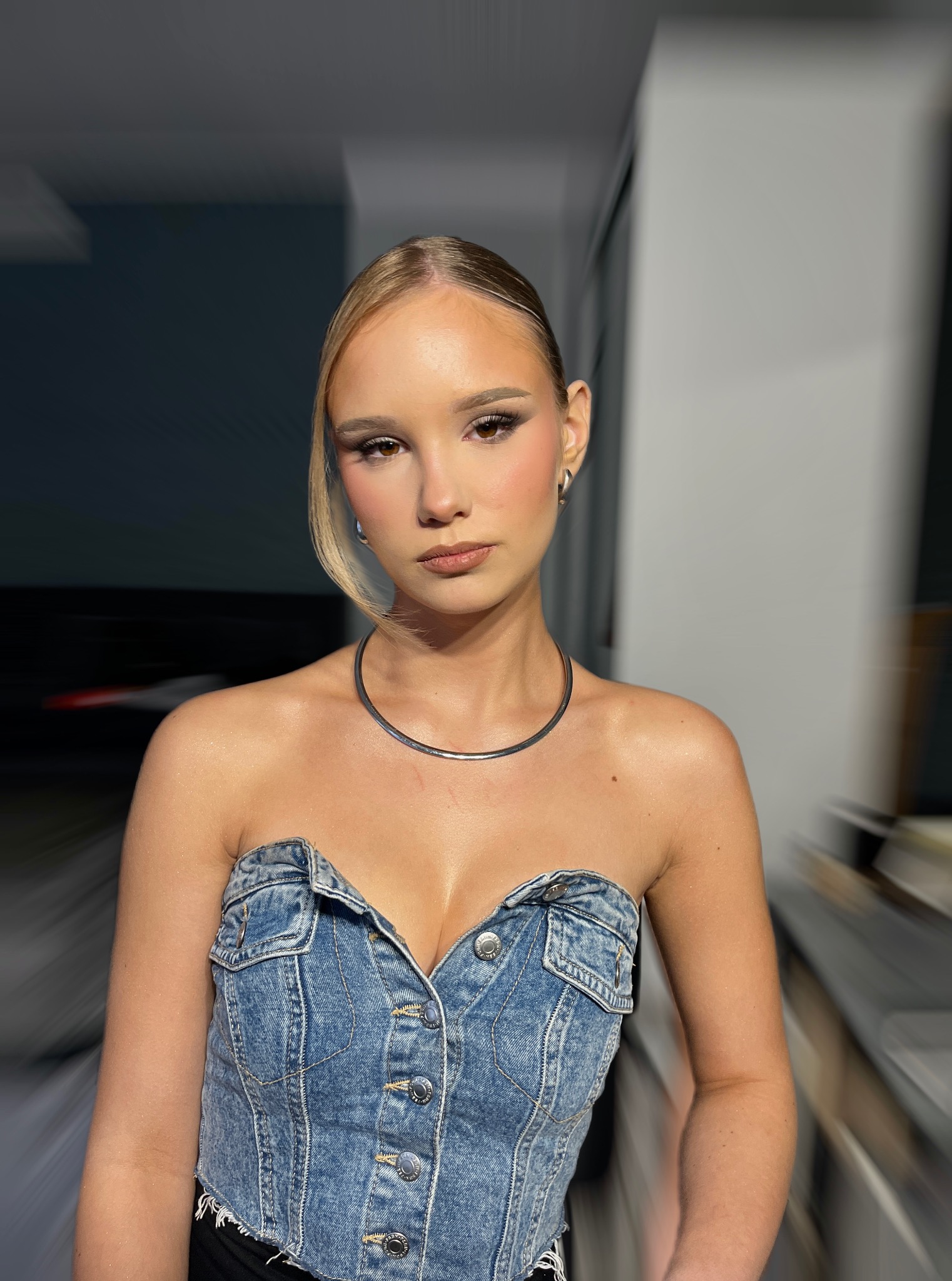 Portret kobiety z delikatnym, profesjonalnym make-upem, prezentujący naturalny efekt. Uwagę zwraca denimowy top bez ramiączek i srebrny naszyjnik.