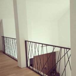 Lubner Schody - Nowoczesne balustrady z czarnych prętów tworzących geometryczny wzór, widoczne z góry. Jasne wnętrze, drewniana podłoga, białe ściany. Minimalistyczny design.