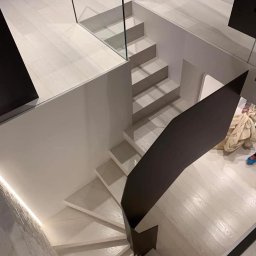 Lubner Schody - Kaskadowe schody z drewnianymi stopniami i szklaną balustradą, widziane z góry. Minimalistyczny design, jasna kolorystyka i nowoczesne wykończenie.