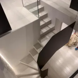 Kaskadowe schody z drewnianymi stopniami i szklaną balustradą, widziane z góry. Minimalistyczny design, jasna kolorystyka i nowoczesne wykończenie.