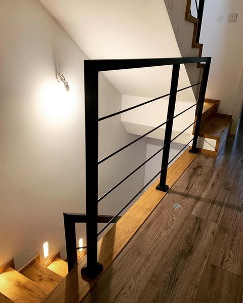 Minimalistyczna, czarna balustrada z poziomymi prętami, zamontowana na drewnianych schodach w jasnym wnętrzu. Widok z góry, oświetlenie punktowe.