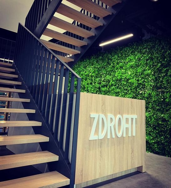 Nowoczesne schody metalowe z drewnianymi stopniami i czarną balustradą w budynku z zieloną ścianą i recepcją z napisem. Ujęcie z dołu.