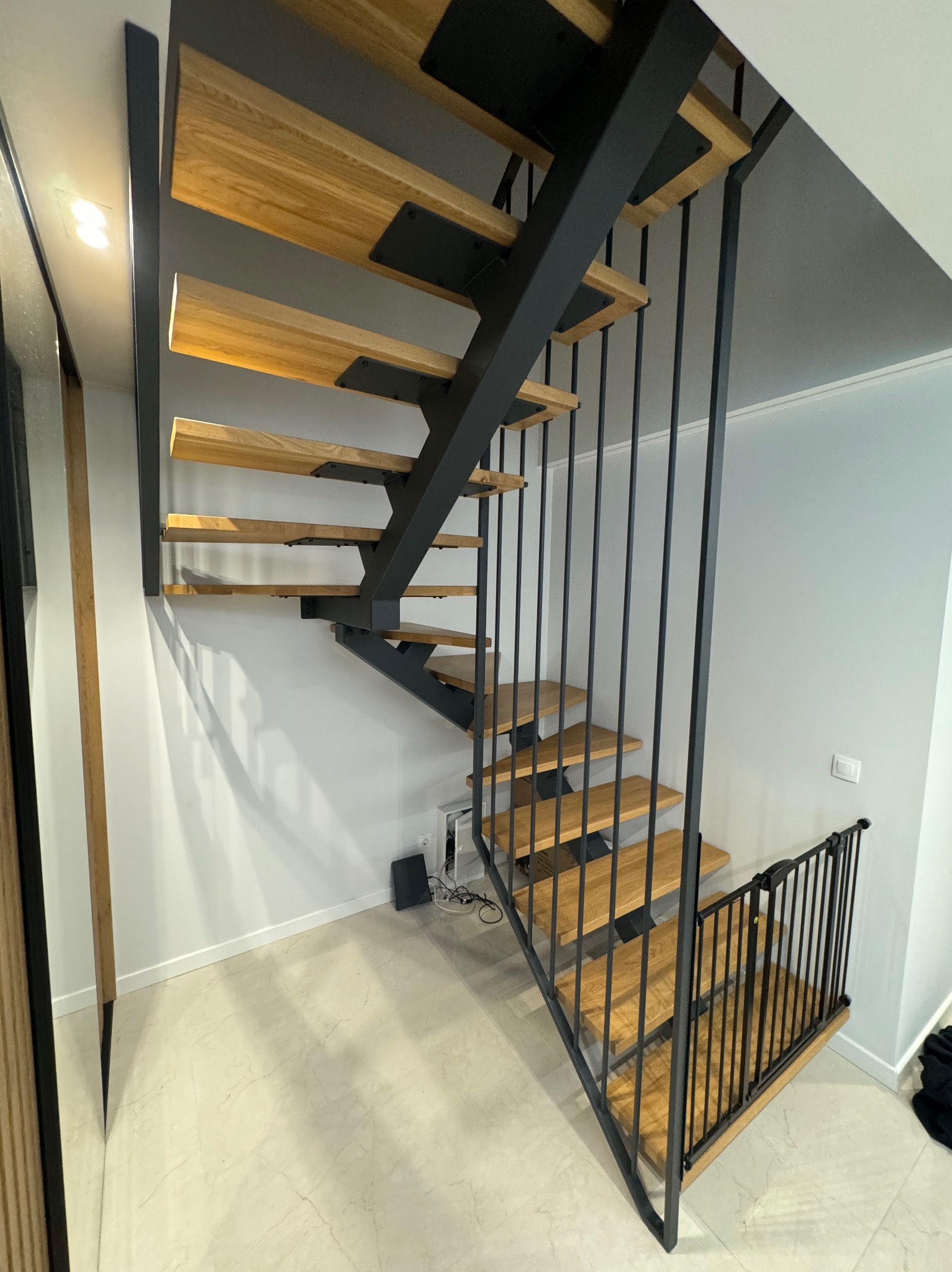 Nowoczesne schody drewniane z czarną metalową konstrukcją, widok z dołu, jasne wnętrze, minimalistyczny design, zabezpieczenie schodów barierką dla dzieci.