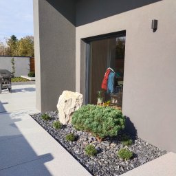 ,, KRAWCZYK '' F. U. H. - Nowoczesny ogród z rabatą przy budynku: kamień, karłowate sosny na czarnym żwirze. W tle widoczny grill i zadbany trawnik. Minimalistyczny design.