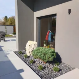 Nowoczesny ogród z rabatą przy budynku: kamień, karłowate sosny na czarnym żwirze. W tle widoczny grill i zadbany trawnik. Minimalistyczny design.