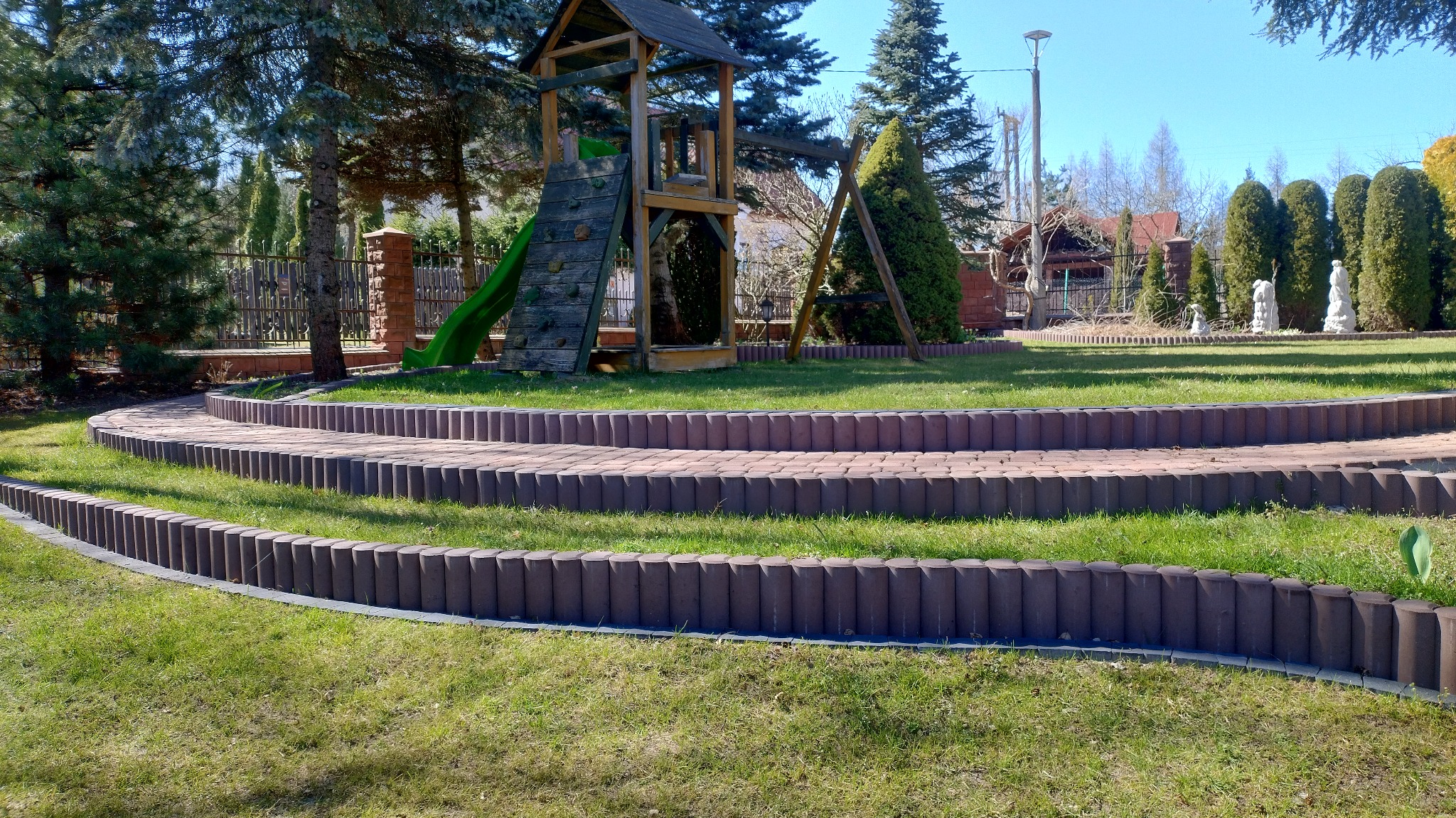 Ogród z trawnikiem i schodami z obrzeżami z kostki, plac zabaw w tle. Układ schodów z kostki tworzy malowniczy krajobraz w ogrodzie.