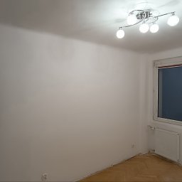 Centrum Edukacji Focus Jakub Mańczyński - Jasne wnętrze po odświeżeniu: białe ściany, parkiet w jodełkę, okno z białymi ramami i czerwonym akcentem, nowoczesna lampa sufitowa. Widoczna część drzwi z żółtą taśmą.