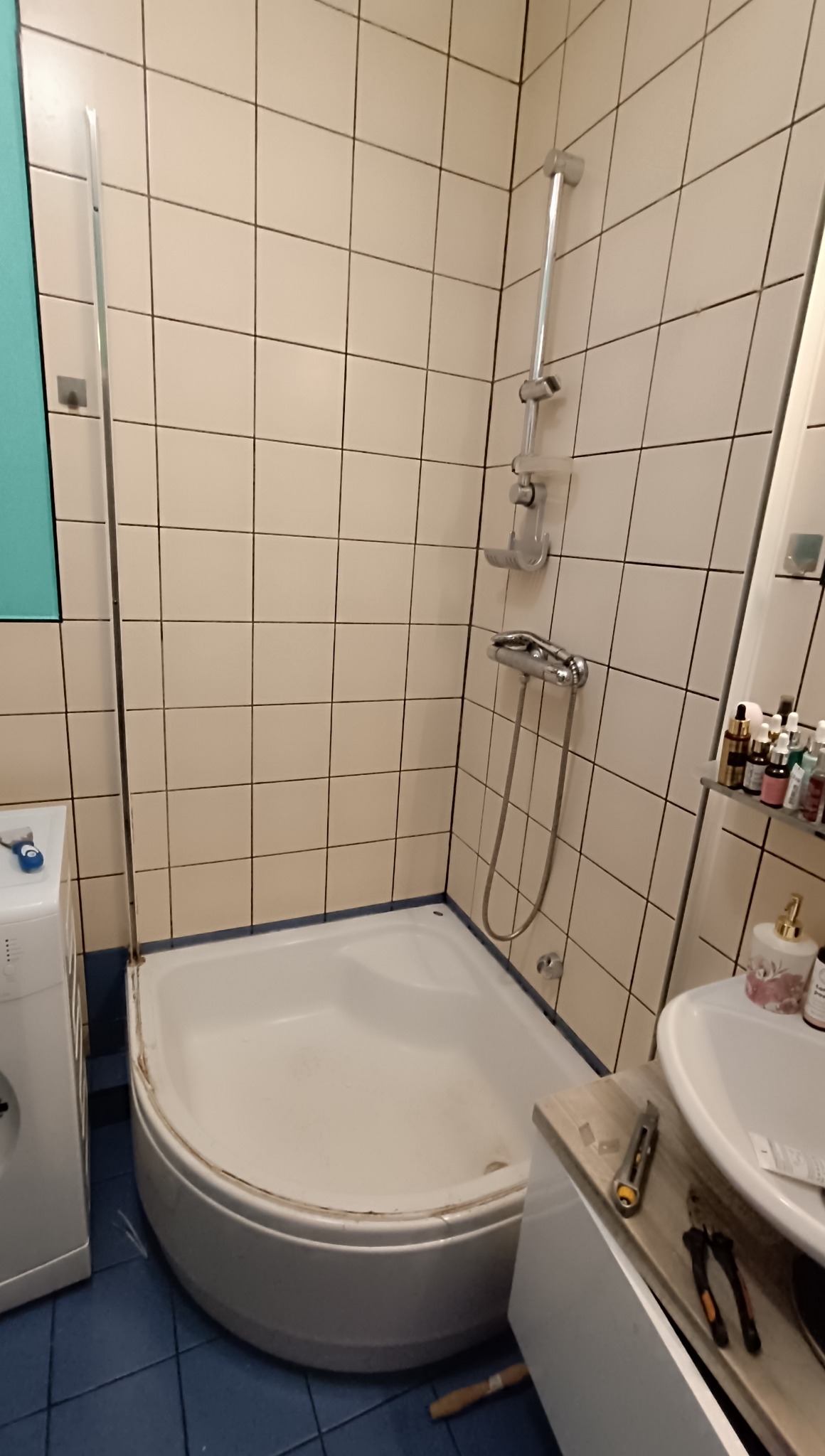 Wyremontowana łazienka z kabiną prysznicową, białe płytki na ścianach i niebieska podłoga. Na blacie leżą narzędzia.